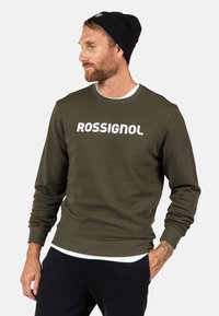Felpa verde oliva con colletto e polsini a coste, caratterizzata dalla scritta bianca in grassetto "ROSSIGNOL" sul petto. Tessuto morbido.