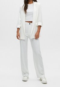 Blazer blanco con mangas remangadas, combinado con una parte superior blanca corta y pantalones de pierna ancha. El calzado son mocasines blancos. Textura de tejido suave.