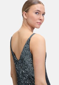 Czarna sukienka z cekinami o dekolcie w kształcie litery V, cienkimi ramiączkami i dopasowanym kroju, prezentująca refleksyjne tekstury oraz skomplikowane zdobienia.