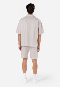 Camicia a maniche corte a righe di colore chiaro e pantaloni corti abbinati. Vestibilità rilassata, tessuto liscio, colletto puntato e tasche laterali.