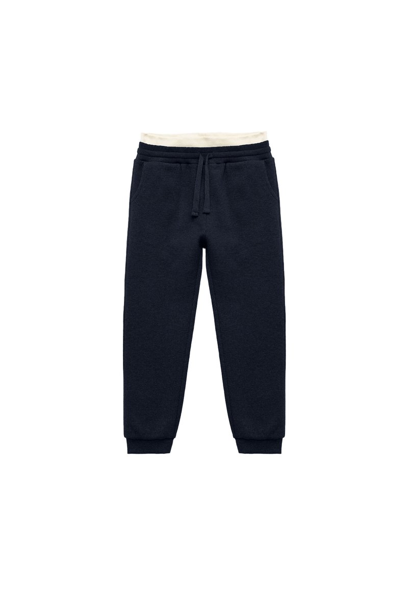 Pantalones de chándal azul marino hechos de un tejido texturizado, con cintura ajustable mediante cordón, banda elástica color crema y puños ajustados en los tobillos.