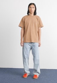 Brown cotton t-shirt with short sleeves, paired with light blue loose jeans and orange sneakers. Plain design, no visible patterns or accents.