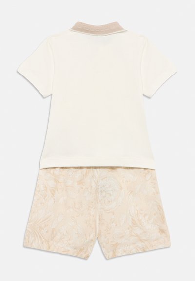 Λευκό πόλο μπλούζα με κοντά μανίκια και γιακά σε ελαφρώς μπεζ υφή, σε συνδυασμό με σορτς στο ίδιο χρώμα, διακοσμημένα με διακριτικό λουλουδένιο μοτίβο σε μπεζ αποχρώσεις.