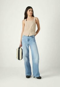 Beige kort topp med en diagonalt sömdetalj, kombinerad med ljusblå utsvängda jeans och en svart-vitrandig väska. Mörka skor fulländar looken.