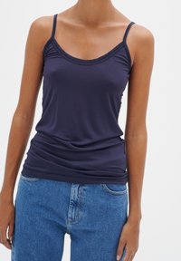 Marinblå ärmlös linne i mjukt, stretchigt material med rundad halsringning och rynkad textur vid nederkanten, parat med blå jeans.