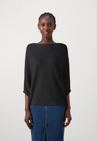 Top noir en tricot côtelé avec un large col et des manches 3/4, associé à une jupe en denim bleu avec une fente centrale.
