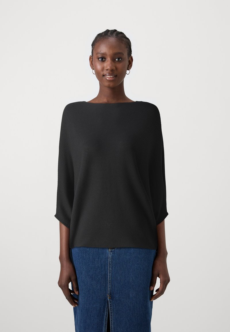 Top noir en tricot côtelé avec un large col et des manches 3/4, associé à une jupe en denim bleu avec une fente centrale.