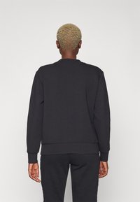 Felpa nera realizzata in morbido materiale, con collo rotondo, polsini e orlo a costine, dal design rilassato. La vista posteriore mostra dettagli minimi.