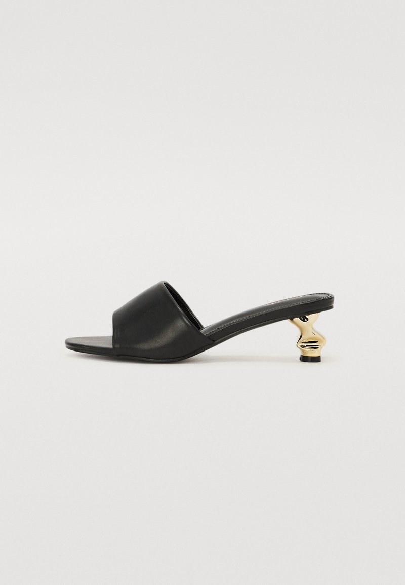 Sandálias em couro preto com o dedo do pé aberto e um salto curvado com acabamento dourado. Sola plana com design minimalista e textura suave.