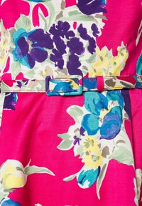 Blommig klänning med en livlig rosa bakgrund, prydd med blå, lila och gula blommor. Inkluderar ett matchande bälte med en rektangulär spänne.
