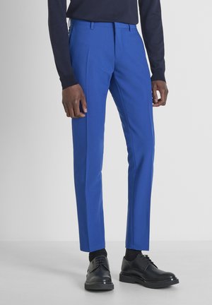 Pantalones azul brillante con un corte entallado, hechos de tela suave. Combinados con zapatos de vestir negros y usados con un suéter oscuro.