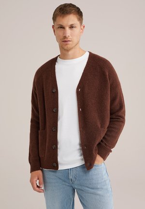 Brown knit cardigan with a textured finish, featuring a V-neck, front pockets, and six black buttons, worn over a white t-shirt.
