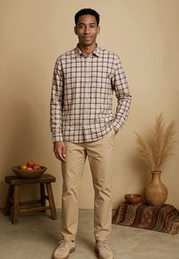 Gestreepte blouse met knopen in beige en marineblauw, gecombineerd met beige broek. De outfit heeft een casual pasvorm, aangevuld met lichtgekleurde schoenen.