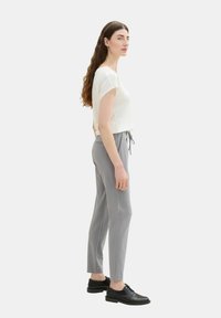 Weißes kurzärmliges Oberteil, hellgraue Jogginghose mit Kordelzug und schwarze Schnürschuhe. Slim-Fit und glattes Material mit schlichtem Design.