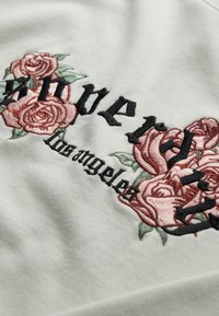 Tessuto di cotone grigio con ricami floreali neri e rosa. Il testo "super" e "los angeles" è incluso in caratteri in grassetto.