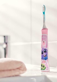 Elektrische tandenborstel met een roze handvat dat cartoonfiguren afbeeldt, een witte en blauwe borstelkop en een knop voor bediening. Zachte textuur.