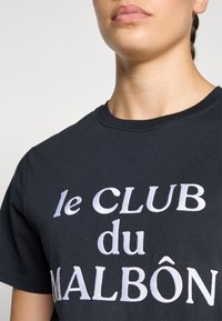 T-shirt in cotone nero con testo ricamato bianco "le CLUB du MALBÔN." Collo tondo, maniche corte, texture liscia, design minimalista.