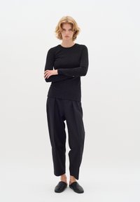 Fekete, hosszú ujjú felső, diszkrét csillámos hatással, laza fekete nadrággal párosítva. Az öltözetet fekete slip-on cipők egészítik ki.