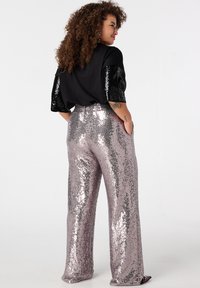 Zwart topje met korte mouwen bezet met pailletten; glanzende, wijde, roze paillettenbroek; losse pasvorm; zichtbare zijzakken; gladde textuur.