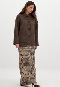 Brown suede jacket with a pointed collar, front buttons, and two patch pockets; paired with a patterned, long skirt featuring animal prints.