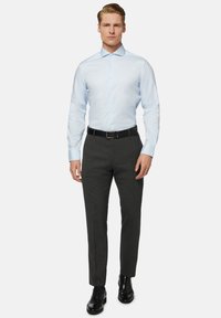 Hellblaues Langarmhemd mit spitzem Kragen, kombiniert mit anthrazitgrauen Hosen und schwarzen Lederschuhen. Details sind Knöpfe am Hemd.