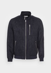 Granatowa zamszowa kurtka z wysokim kołnierzem, przednim zamkiem błyskawicznym oraz dwiema zapinanymi na zamek kieszeniami po bokach. Prążkowane mankiety i dół dodają faktury i struktury.