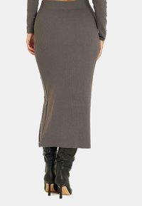 Jupe midi grise côtelée avec des accents de boutons sur le côté, présentant une coupe ajustée et une légère fente sur le côté. Associée à des bottes noires à talons aiguilles montantes.