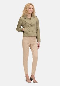 Olijfgroene dubbelzijdige cropped jas met knopen, gecombineerd met beige aansluitende broek en gespenhakken. Soepele stof en gestructureerd ontwerp.