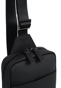 Borsa a tracolla nera realizzata in tessuto testurizzato con scomparti con zip, tracolla regolabile e dettagli in metallo.