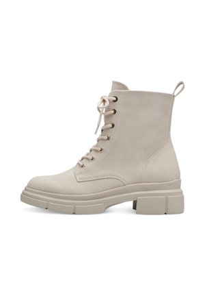 Beige Knöchelstiefel aus einem glatten, wildlederähnlichen Material, runder Zehenpartie, mit Schnürung an der Vorderseite, goldenen Ösen und einer groben Gummisohle. Mit Zuglasche an der Rückseite.