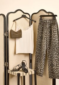 Camisole crème avec bordure en dentelle, pantalon imprimé animal, sac à main noir à perles, et sandales noires à lanières exposés sur un tabouret en bois derrière un paravent.