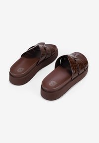 Sandali marroni slip-on con una texture in motivo coccodrillo. Presentano ampi cinturini incrociati e una suola piatta spessa e imbottita.