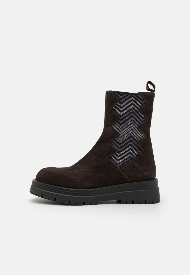 Stivaletto alla caviglia in suede marrone con un pannello in tessuto a zigzag testurizzato, punta arrotondata e suola nera spessa. Presenta un inserto per facilitare la calzata.