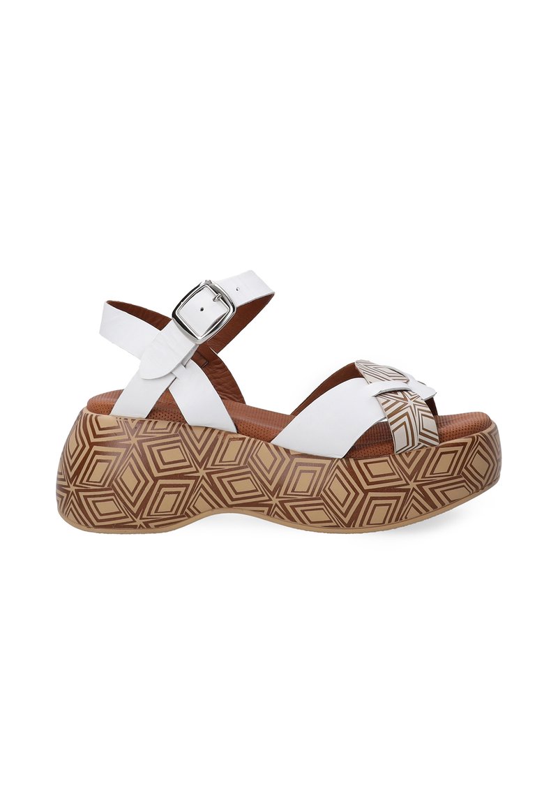 Weiße Plateausandalen mit einem Kreuzriemen-Design, ausgestattet mit einer silbernen Schnalle. Die Sohle hat ein geometrisches braunes Muster und eine strukturierte Innensohle.