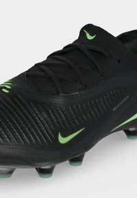 Μαύρα ποδοσφαιρικά παπούτσια Nike VenomSkin με πράσινες λεπτομέρειες, κορδόνια και εμφανείς τάπες σε απλό φόντο.