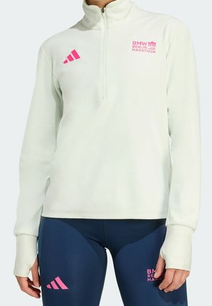 Osoba nosząca biały, rozpinany top z długim rękawem i granatowe legginsy, oba z różowymi logo BMW Berlin Marathon i Adidas.