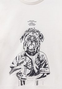 T-shirt bianco con un'illustrazione grafica nera di un bulldog che tiene in bocca una palla da rugby, accompagnata da testo relativo ai successi sportivi.