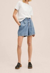 Pantalones cortos de denims de cintura alta y bolsillos frontales, en azul claro. Combinados con una camiseta blanca sencilla y zuecos negros con suelas de madera.