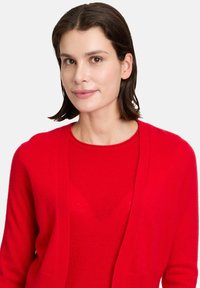 Cardigan rouge avec design à devant ouvert. Fabriqué en matériau doux, présentant une texture côtelée et des manches longues. Assorti avec un haut rouge assorti.