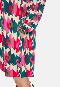 Bunt gemustertes Kleid mit rosa, grünen und beigen geometrischen Formen sowie Akzenten aus Leopardenmuster an den Ärmelabschlüssen und Seitentaschen.