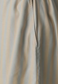 Lightweight fabric featuring vertical stripes in muted blue and beige. The material has a soft texture with visible stitching along the seams.
