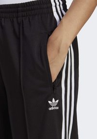 Svarta träningsbyxor med vit tre-stripes design, elastisk midja och sidfickor. Har ett broderat Adidas-logotyp på underbenet.
