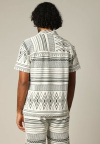 Kortemouw blouse met een geometrisch zwart-wit patroon, waaronder strepen en diamanten, gemaakt van lichtgewicht stof.