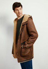 Brązowa skórzana kurtka z kapturem i kołnierzem wyłożonym sztucznym futrem, z zamkiem błyskawicznym i zapięciami na guziki, bocznymi kieszeniami oraz fakturowanymi rękawami.