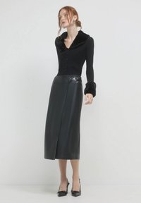 Schwarzes Langarmoberteil mit Kunstfellkragen, kombiniert mit einem hoch taillierten schwarzen Lederrock mit einem vorderen Schlitz und metallischen Gürtelakzenten.