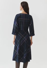Robe à carreaux bleu marine avec des manches trois-quarts, comportant des lignes colorées en vert, rose et bleu. Longueur mi-mollet, coupe décontractée.