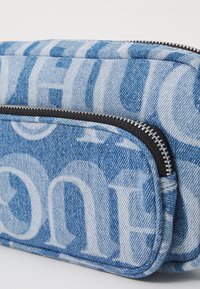 Nieprzemakalna saszetka z niebieskim i białym wzorem tekstowym, wyposażona w czarny zamek błyskawiczny i teksturowany materiał. Kompaktowy prostokątny kształt z przednią kieszonką.