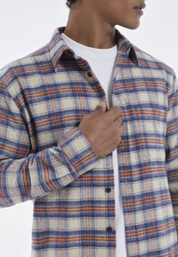 Geruite button-up shirt in roomkleur, marineblauw en rood; gemaakt van textuurstof met een opgeklapte kraag en knoopmanchetten.