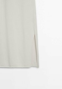 Pull gris clair avec un motif en maille texturée et une fente latérale. La forme est décontractée, avec un ourlet droit et une finition en tissu doux.