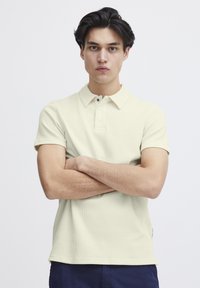 Lys gul teksturert polo-skjorte med korte ermer og krage, med tre knapper ved halsen og rett kant.